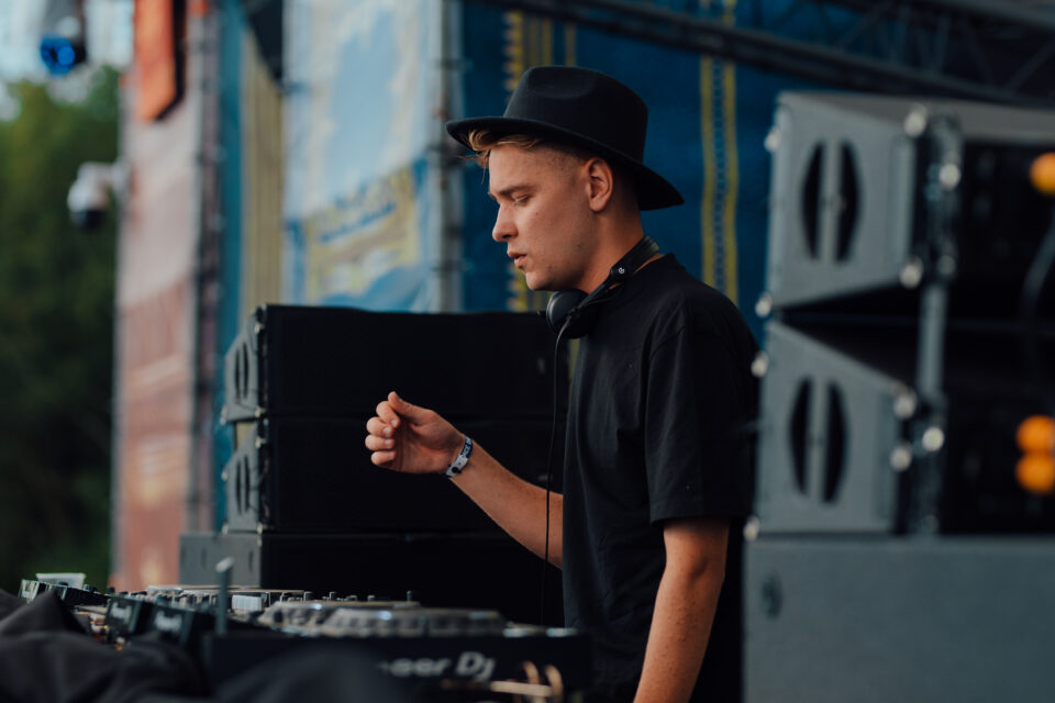 Voltage in a black hat, side on at the decks on an outdoor festival stage