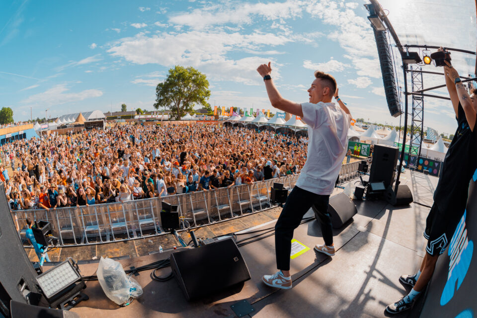 Voltage giving a thumbs up from the stage to a big festival crowd on a sunny day