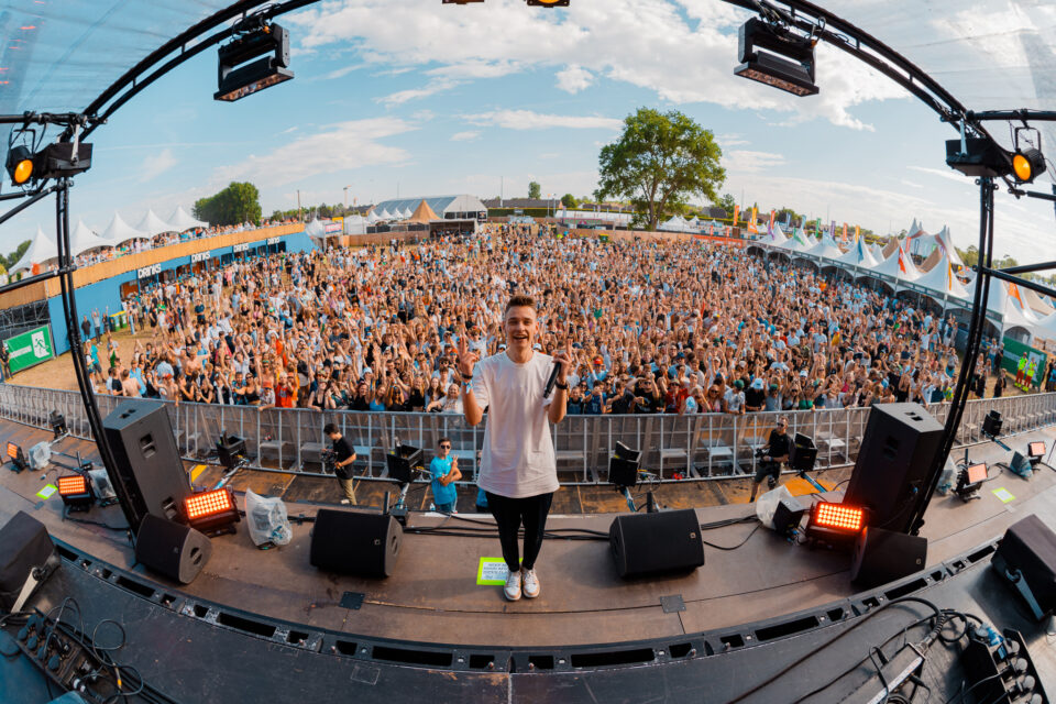 Voltage on stage with a microphone, making a peace sign in front of a huge festival crowd