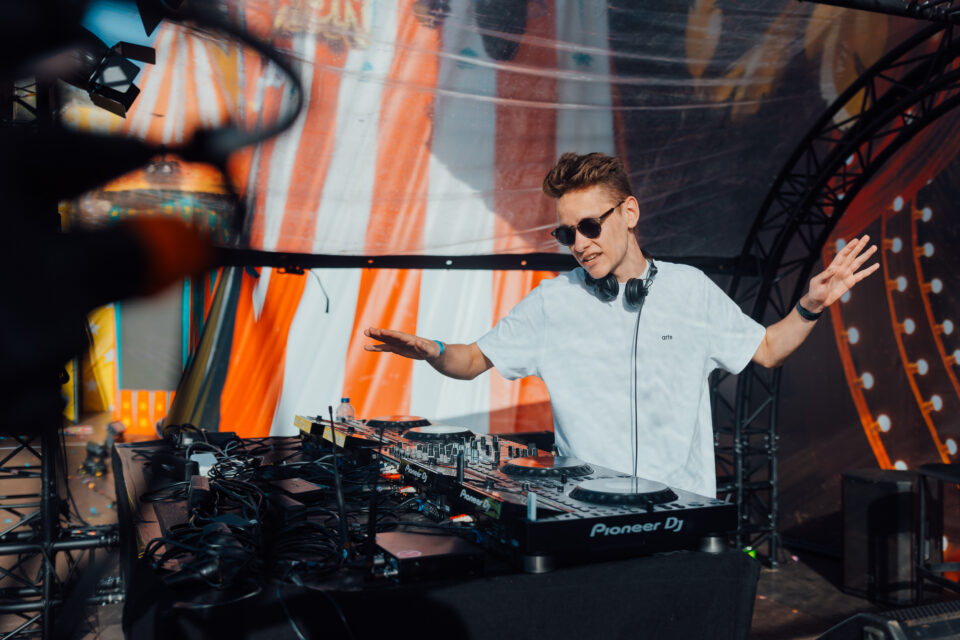 Voltage at the decks in sunglasses and a white T-shirt in front of an orange striped backdrop